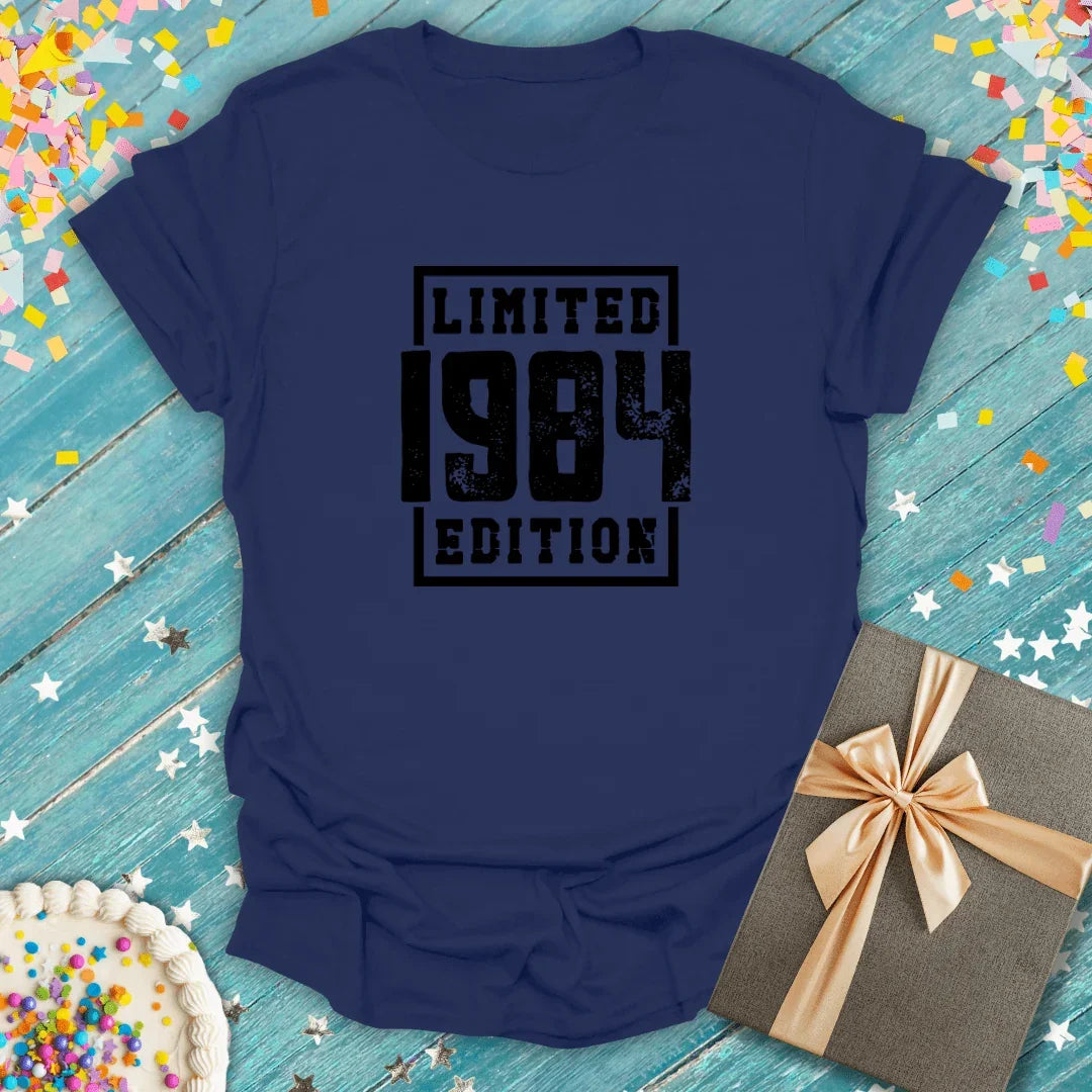 Navy blue 'Limited 1984 Edition' tee on teal wood with confetti, cake, and gift—perfect for birthdays or milestones.