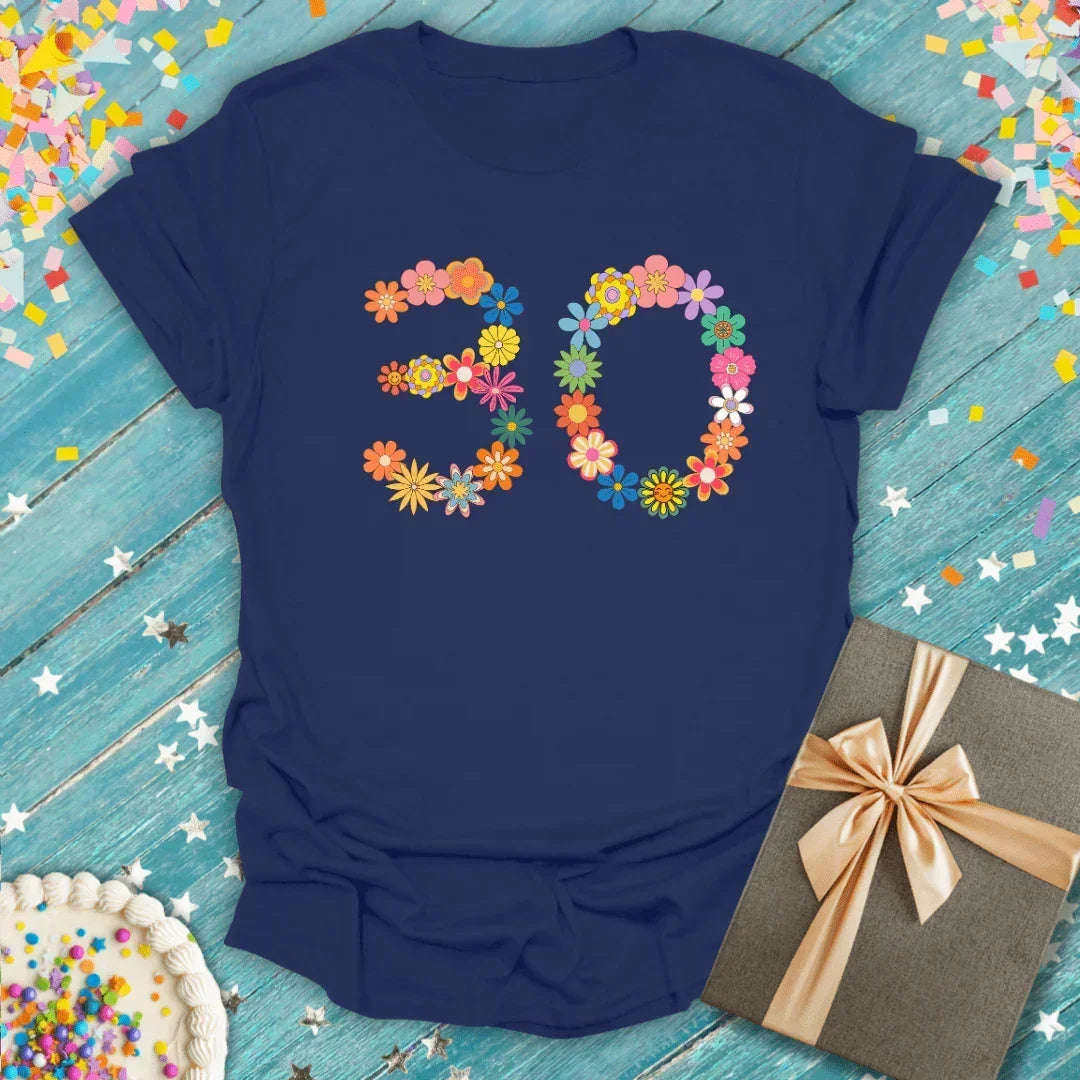 Navy blue 30th birthday tee with colorful floral number design, gift box, and cake on confetti background