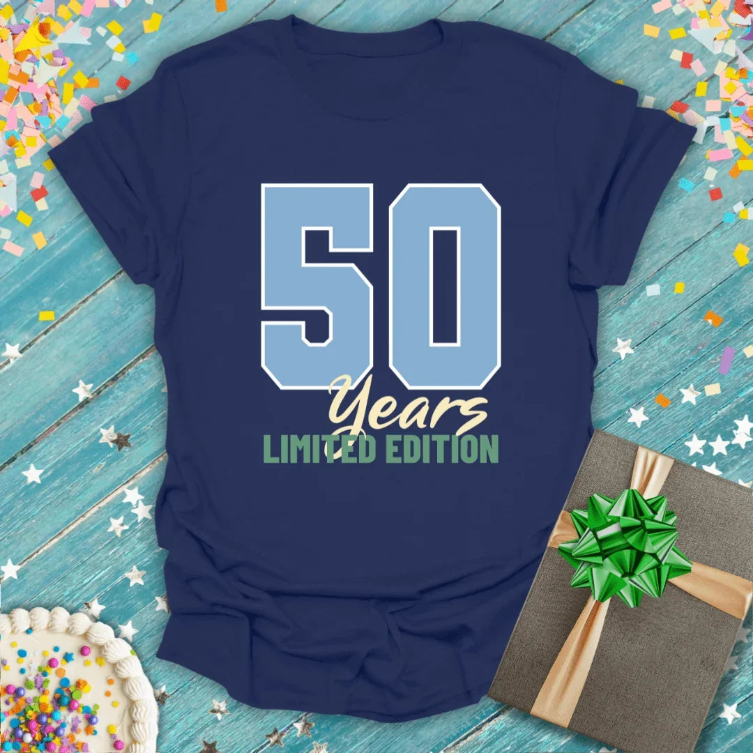 Navy 50 Years Limited Edition birthday tee with confetti, cake, and gift on wood background