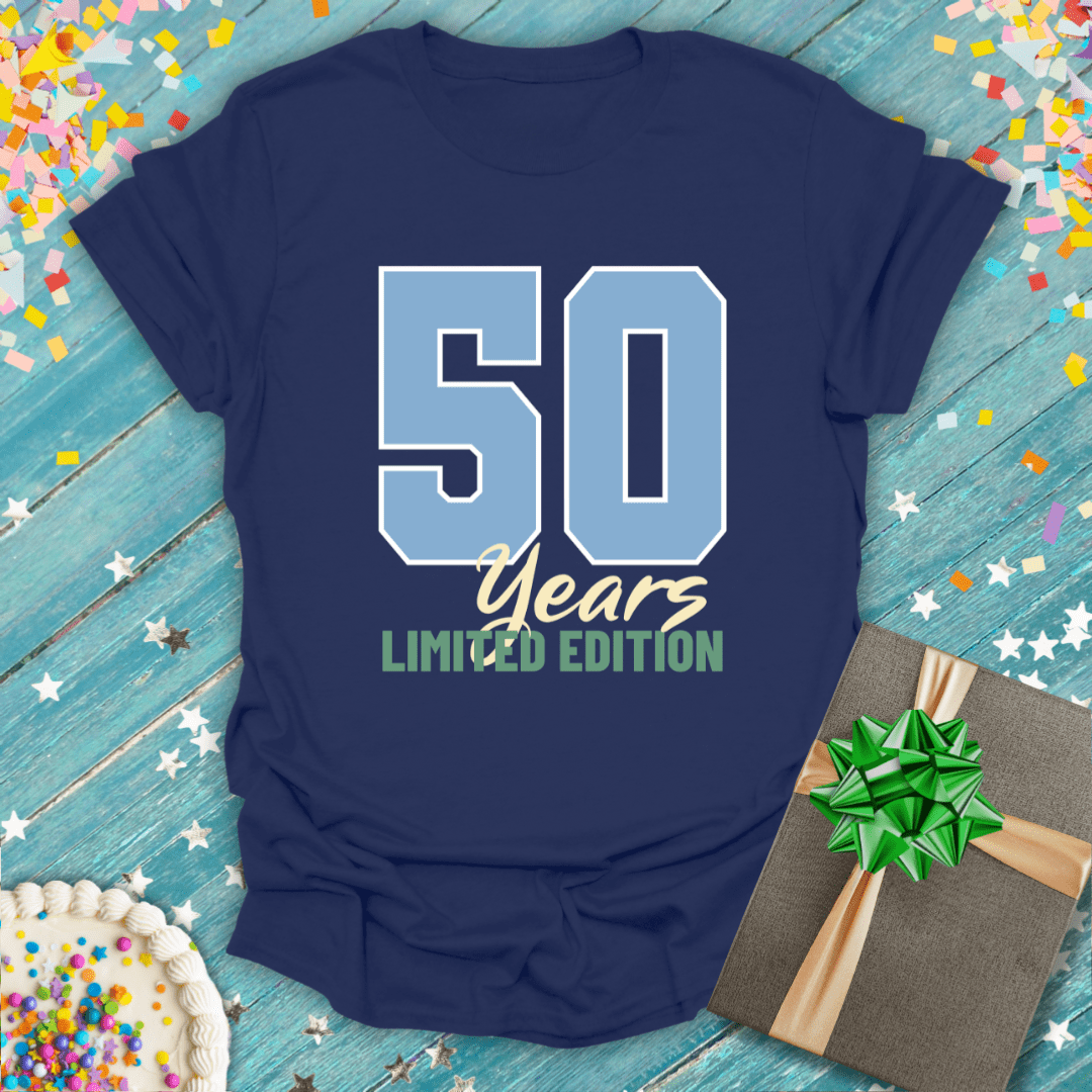 Navy 50 Years Limited Edition birthday tee with confetti, cake, and gift on wood background