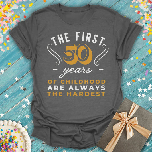 Funny 50th birthday t-shirt on blue wood table with confetti, cake, and gift box.