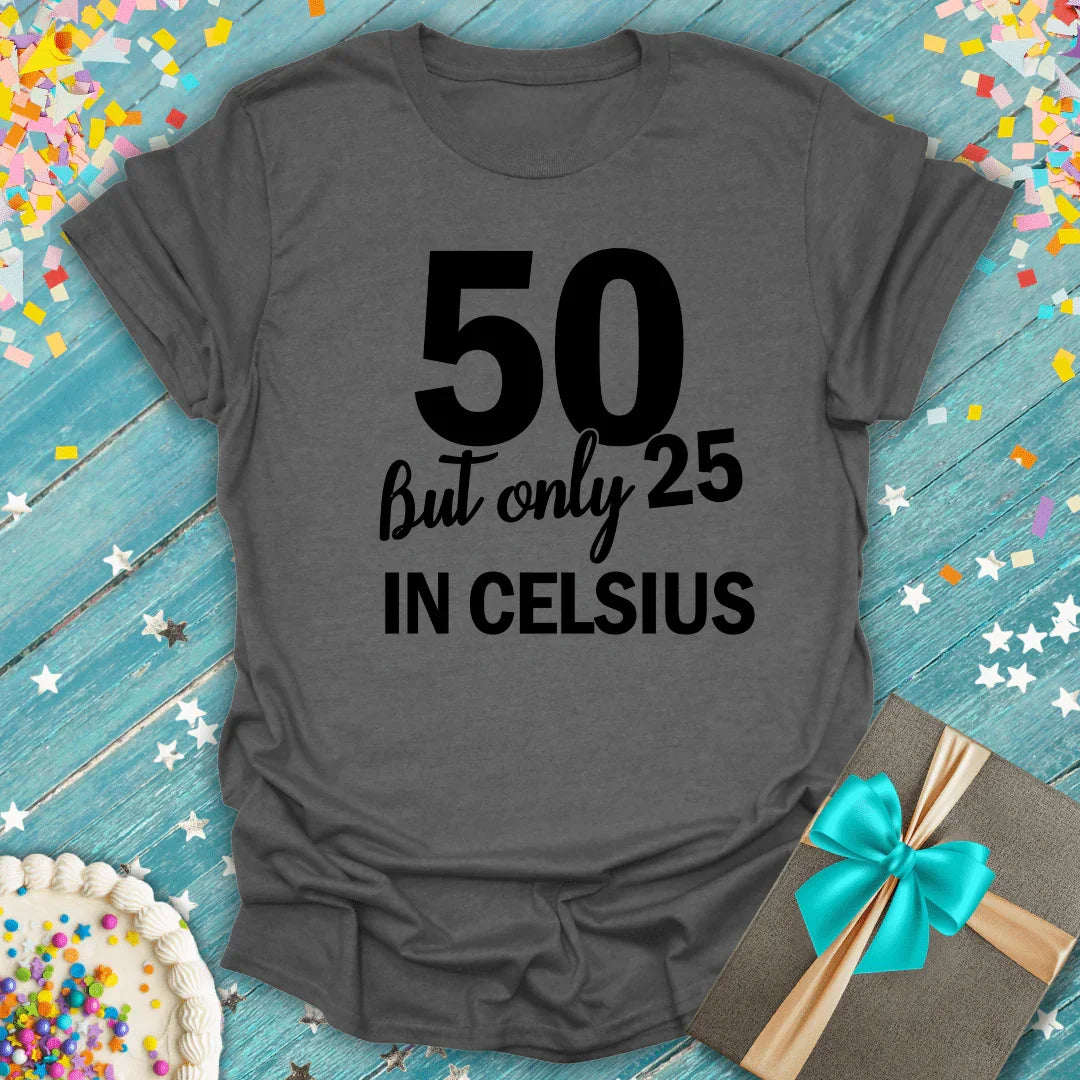 Gray 50th birthday tee saying '50 but only 25 in Celsius' with cake, gift, and confetti on blue wood