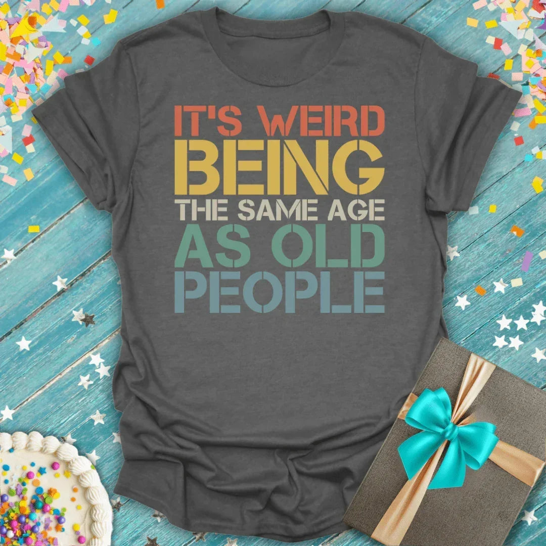 Funny birthday tee in Charcoalsaying 'It's weird being the same age as old people' with cake and gift, perfect for milestones.