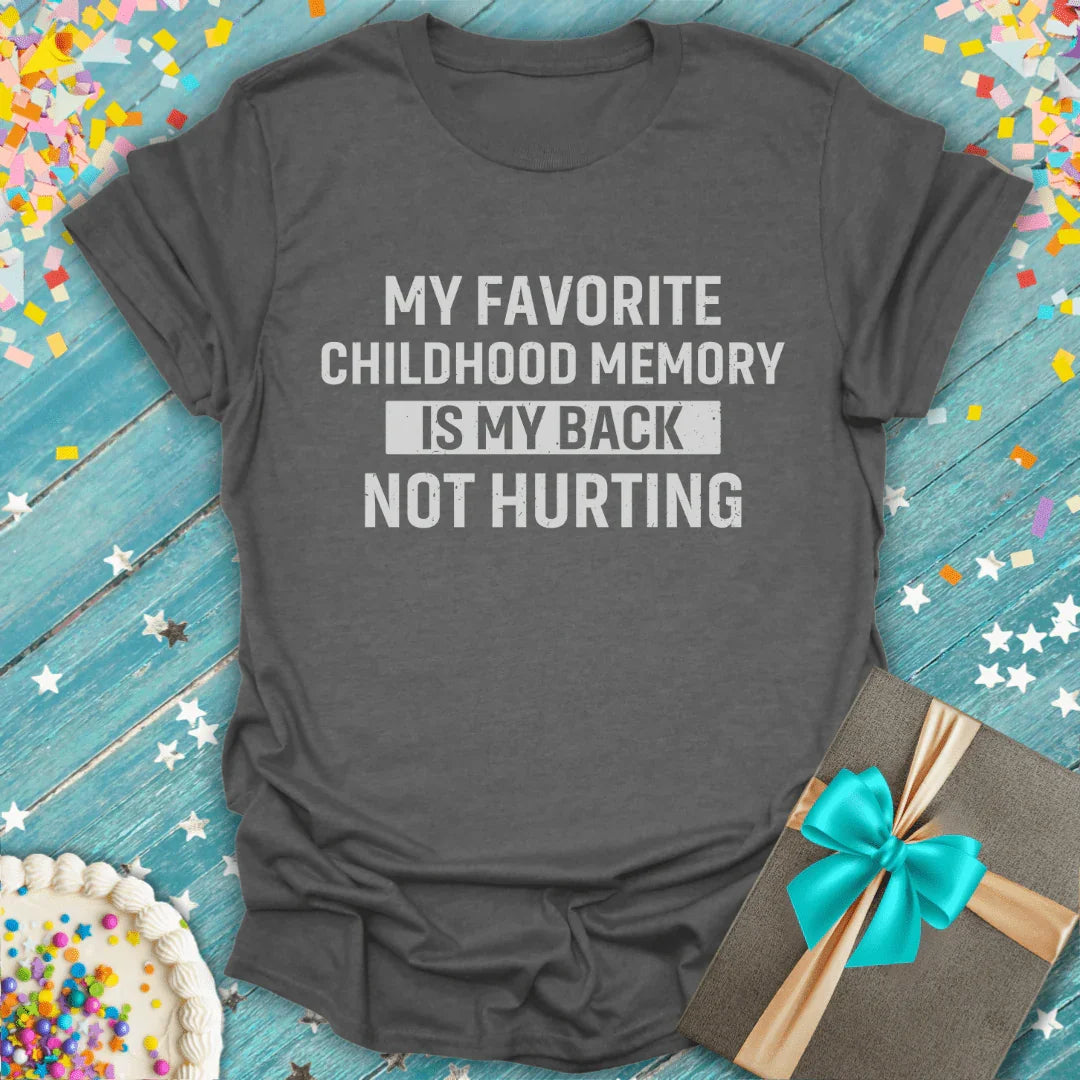 Funny retro T-shirt reading 'My favorite childhood memory is my back not hurting', surrounded by confetti, cake, and a gift on a blue wooden background.