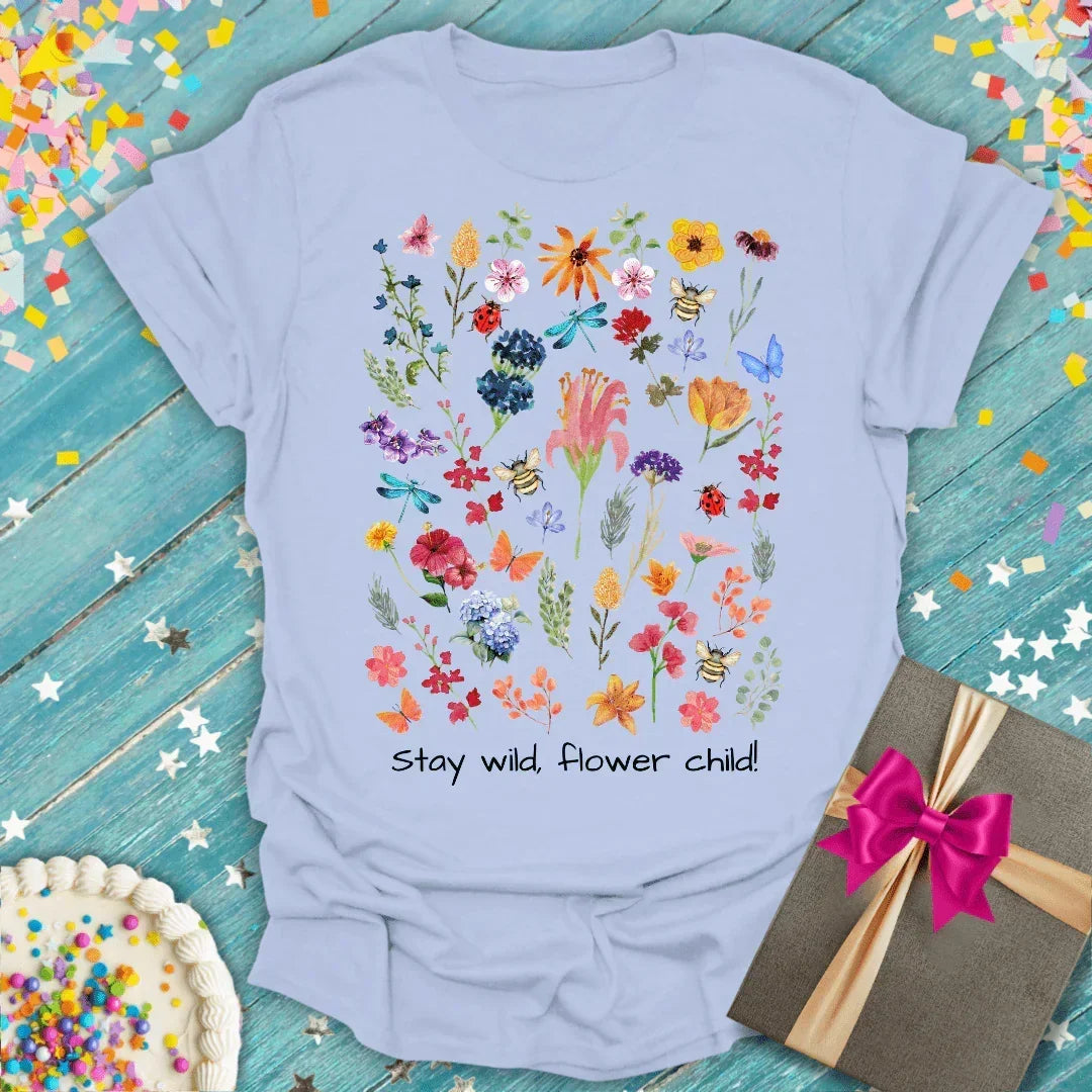 Light blue t-shirt with colorful floral and bee print, 'Stay wild, flower child!' text, gift box and cake nearby