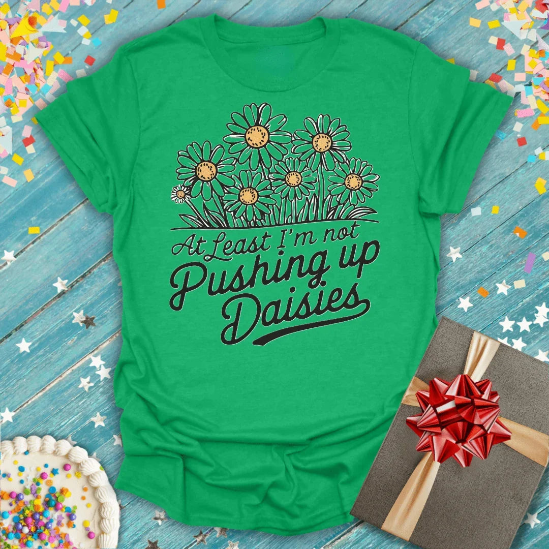 Green t-shirt with 'At Least I'm not Pushing up Daisies' text and daisy graphic, gift box and cake nearby