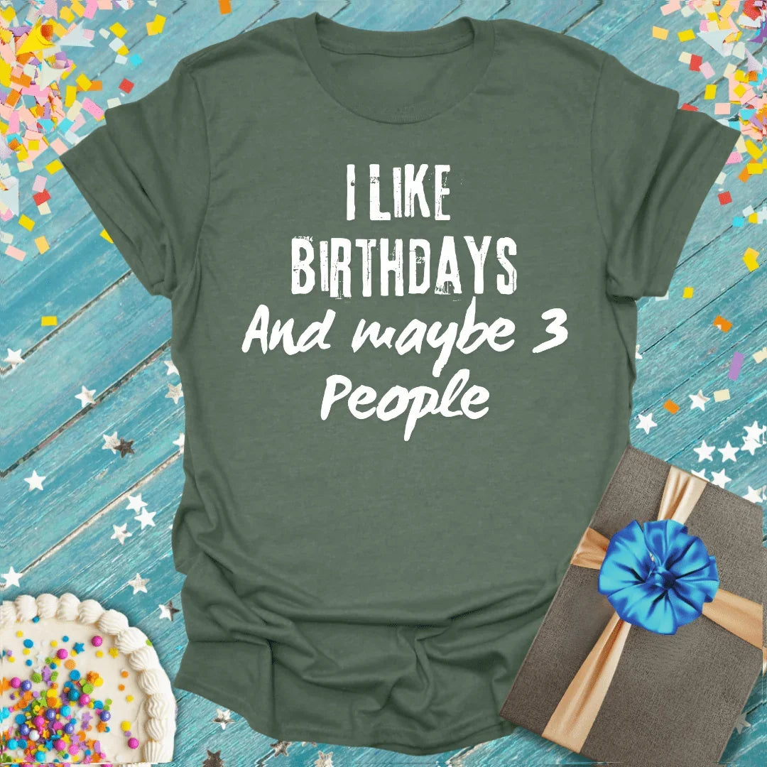 Green birthday tee saying 'I like birthdays and maybe 3 people' with cake, gift, and confetti