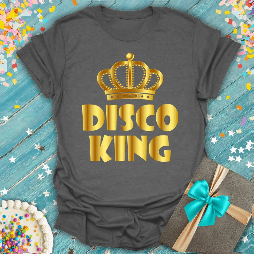 Gray 'Disco King' tee with gold crown, birthday cake, gift box, and confetti on blue wood background