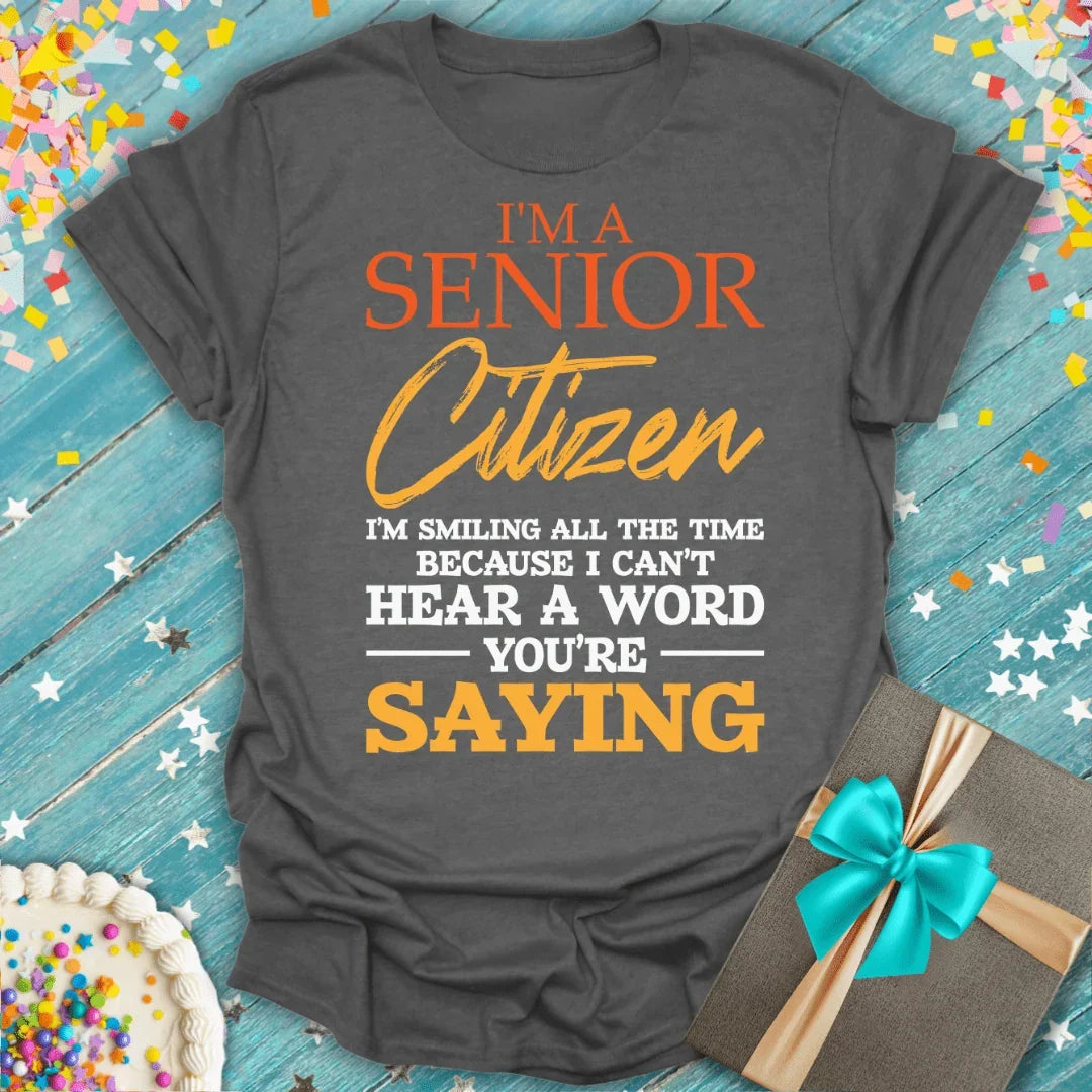 Funny senior citizen t-shirt with bold text, birthday cake, and gift box on blue wood background