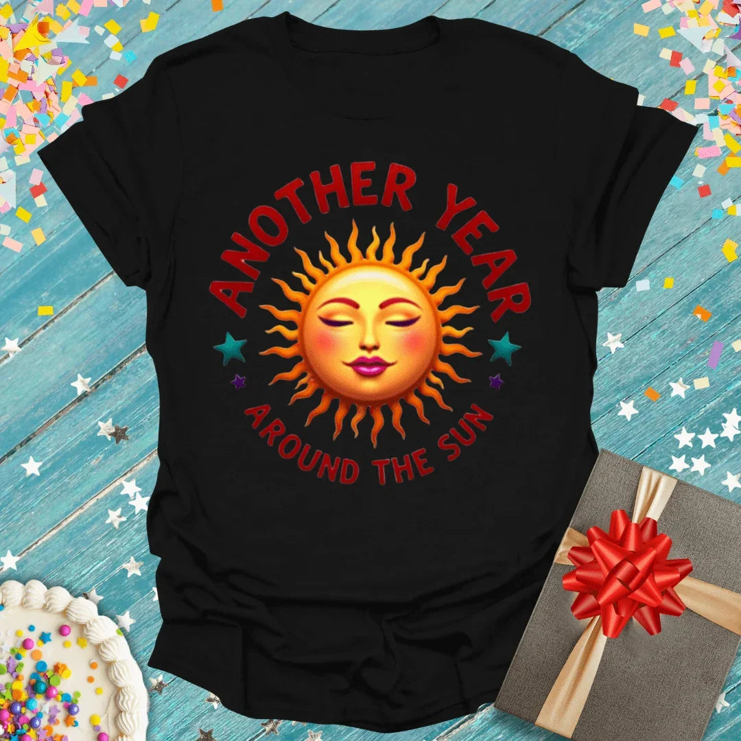 Black birthday tee with 'Another Year Around the Sun' sun graphic, gift box, and cake on blue wood