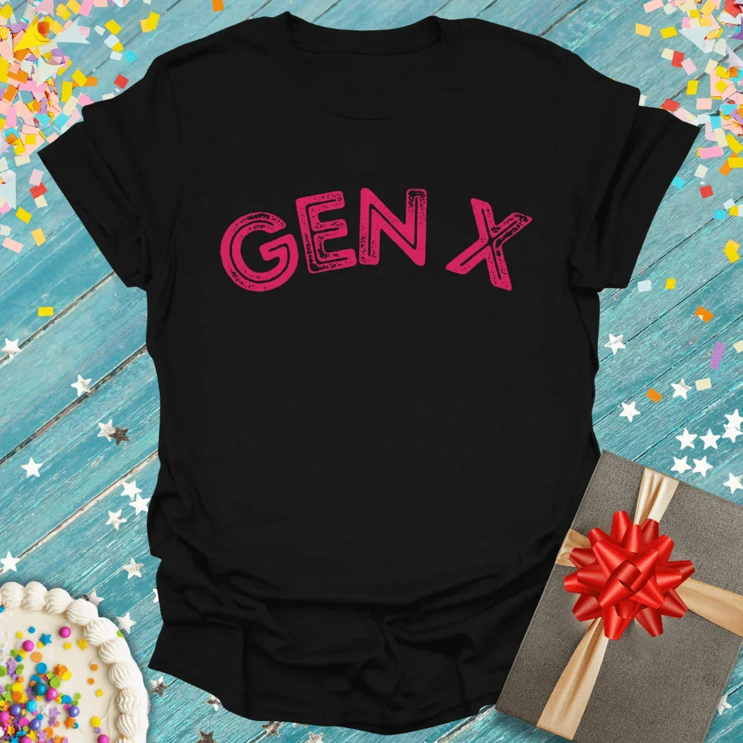 Black Gen X t-shirt with pink graphic, birthday cake, gift box, and confetti on blue wood background