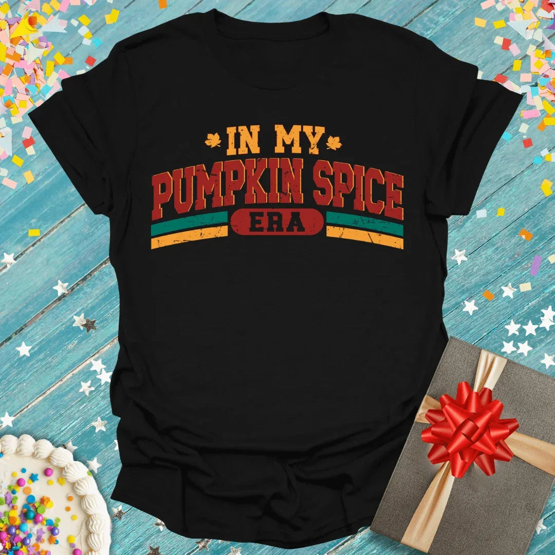Black 'In My Pumpkin Spice Era' tee with fall leaves, gift box, and cake on blue wood background