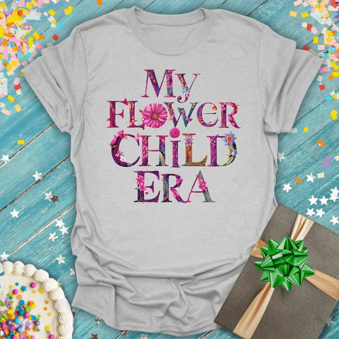 My Flower Child Era tee with floral lettering, birthday cake, and gift on blue wood background