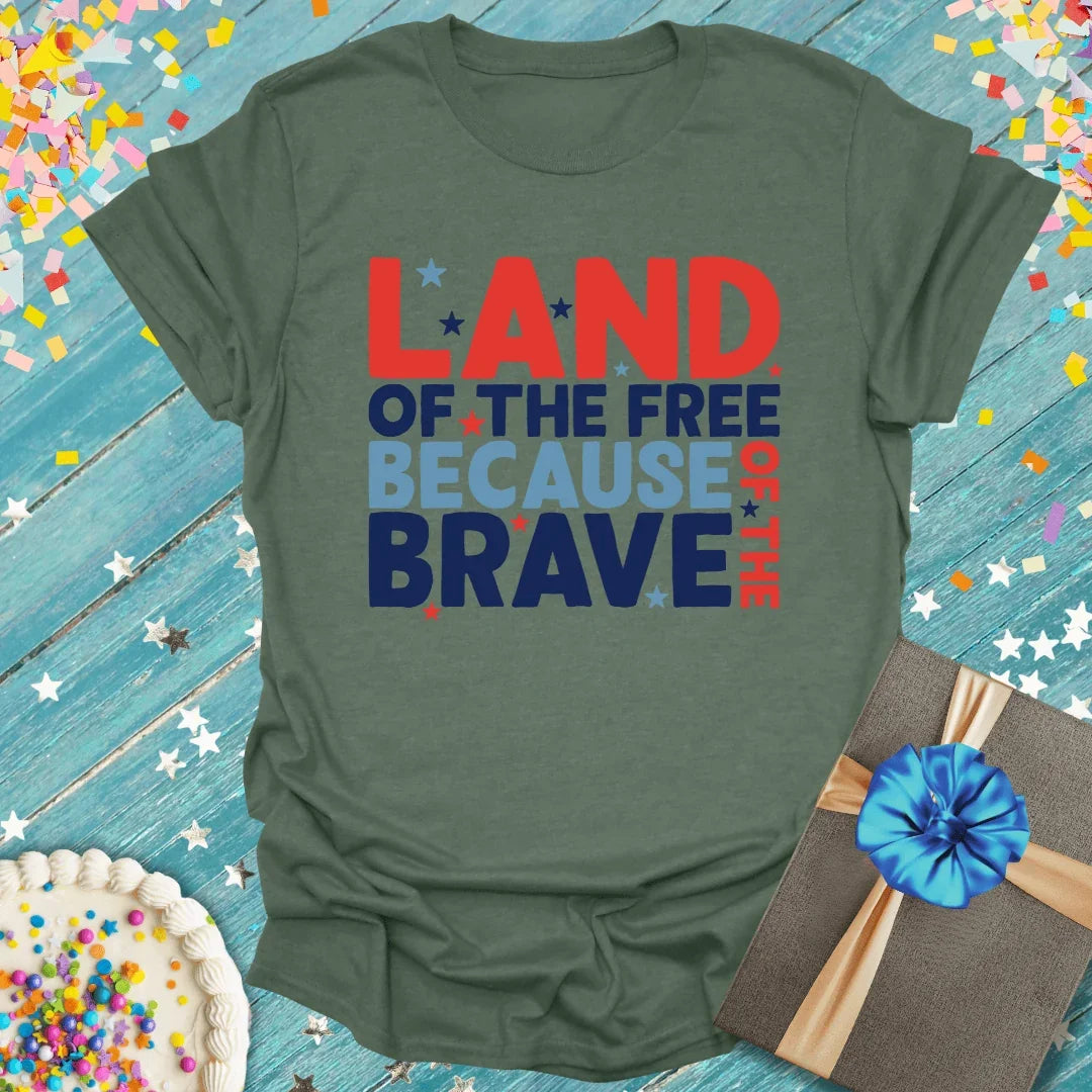 Green tee with 'Land of the Free Because of the Brave' text, stars, gift box, and cake on blue wood