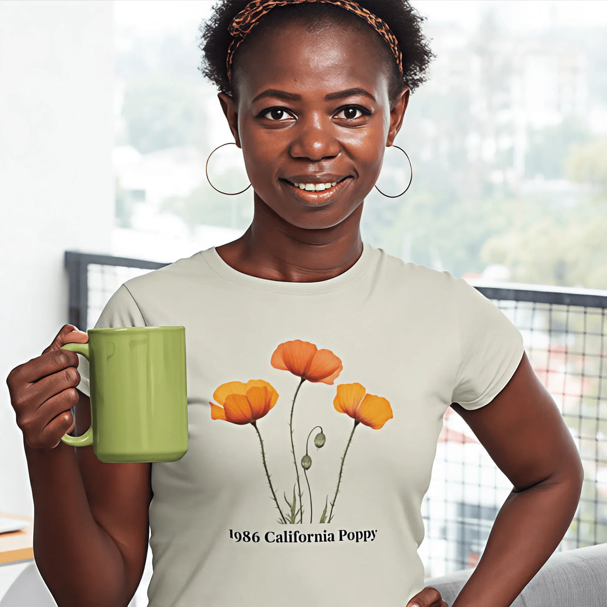 Woman wearing 1986 California Poppy tee, holding green mug, smiling indoors