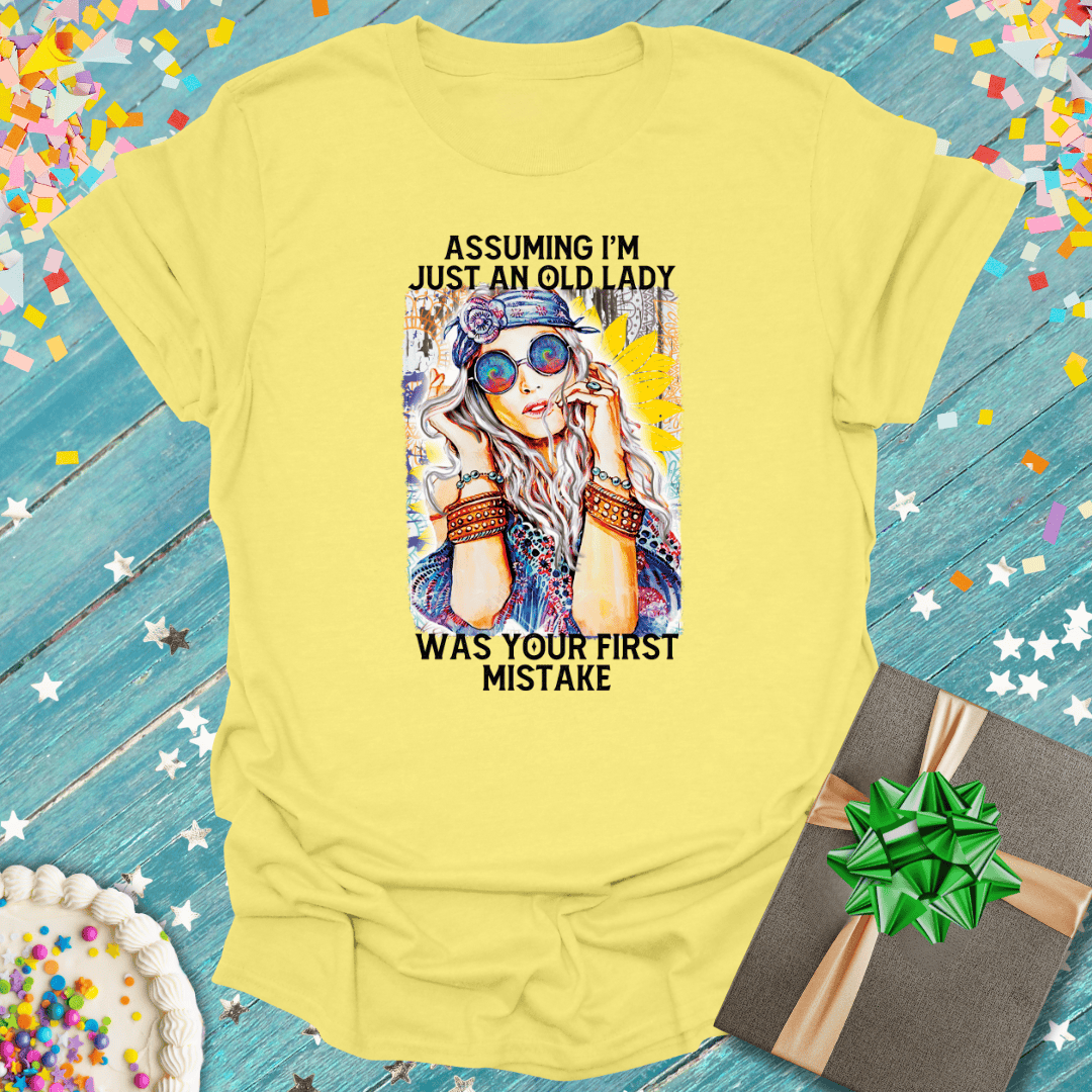 Yellow tee with bold graphic: 'Assuming I'm just an old lady was your first mistake' — perfect for birthdays, gifts, or fun trips.