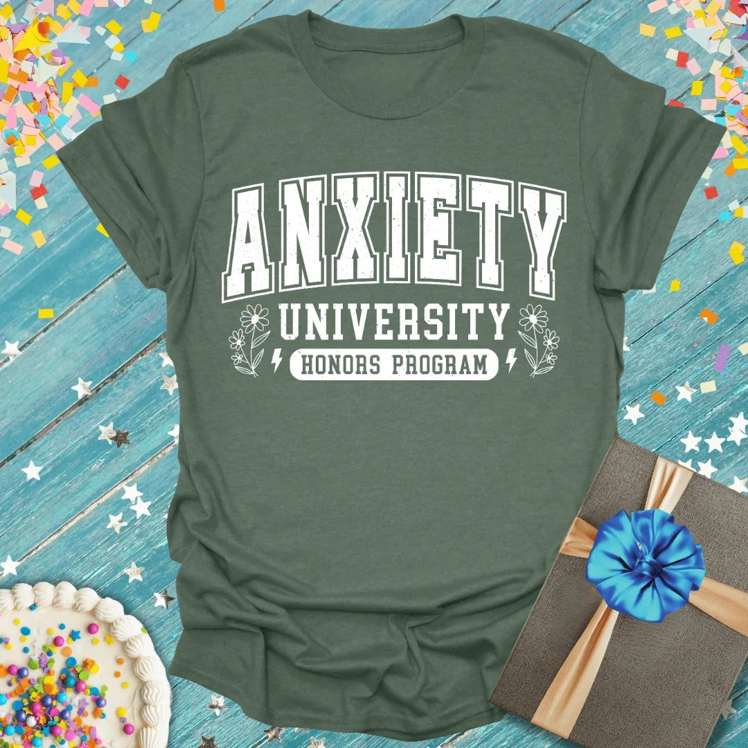 Military Green t-shirt with 'Anxiety University Honors Program' text on a blue wooden surface with confetti.
