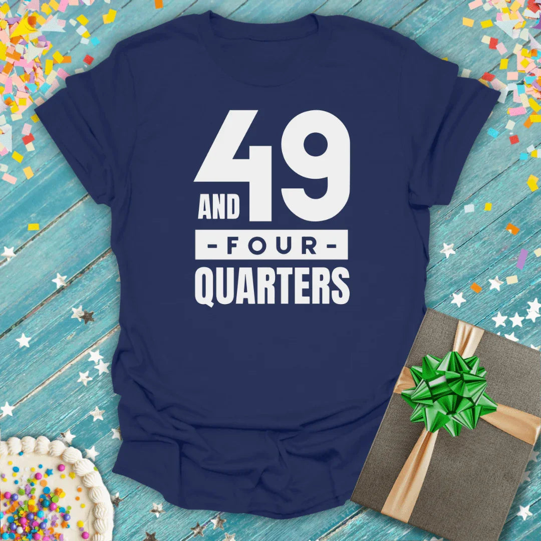 Navy 49 and Four Quarters birthday tee with cake, gift, and confetti on blue wood