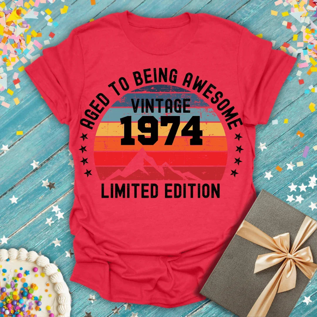 Red vintage 1974 birthday tee, 'Aged to Being Awesome,' limited edition, with cake & gift on blue wood