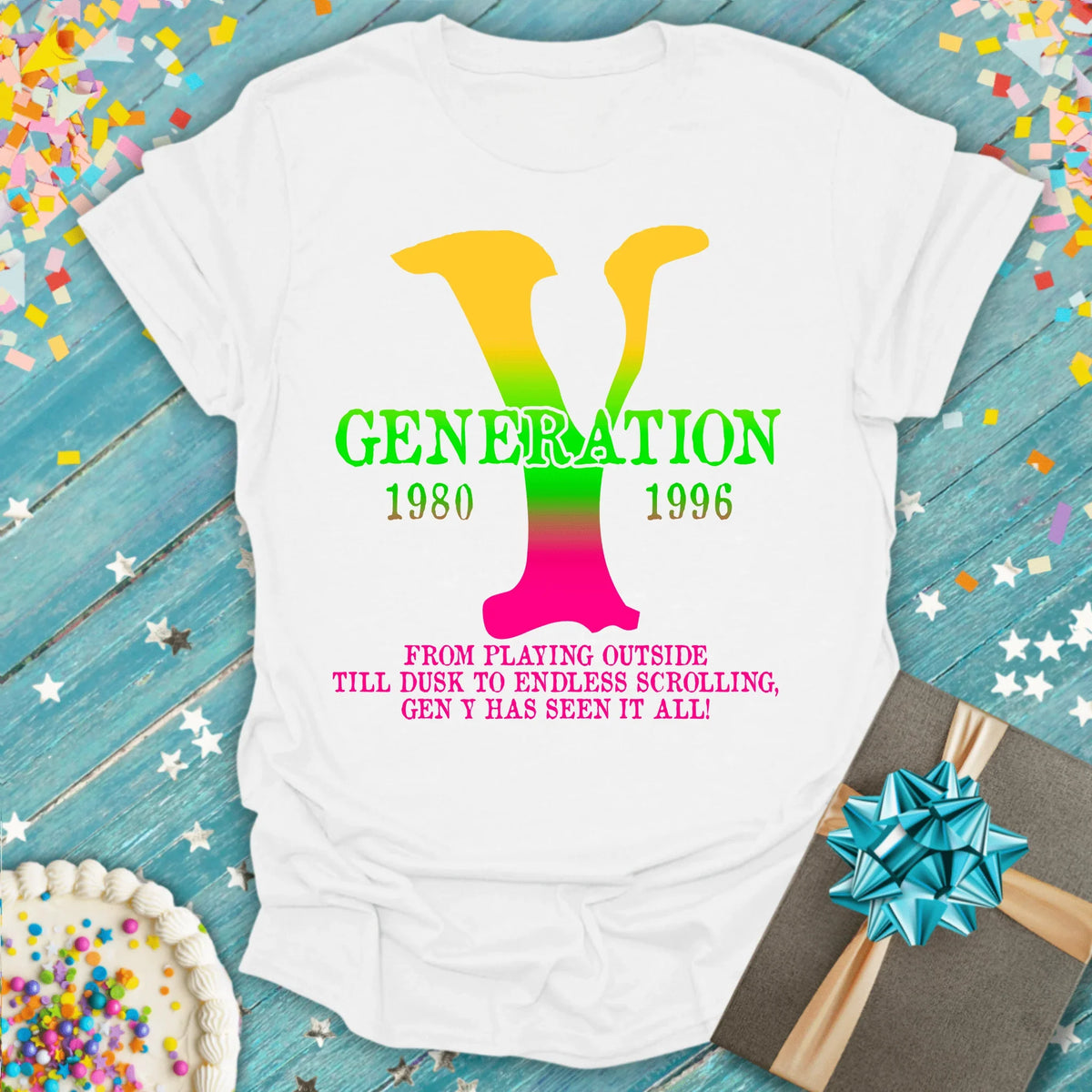 White Generation Y tee with rainbow 'Y', 1980-1996 text, birthday cake & gift on blue wood background