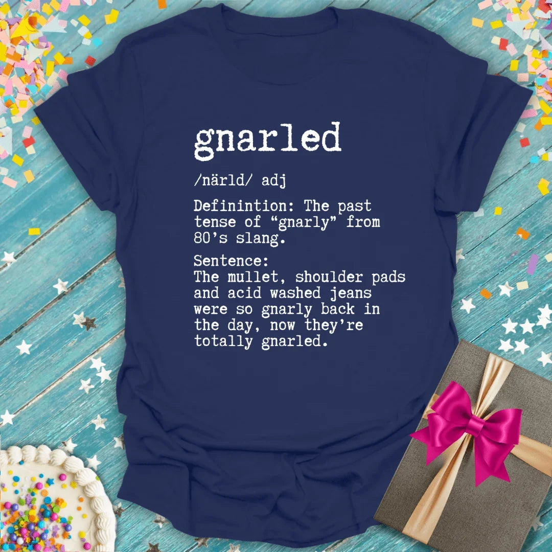 Navy tee with 'gnarled' 80s slang definition, birthday cake, gift box, confetti on blue wood