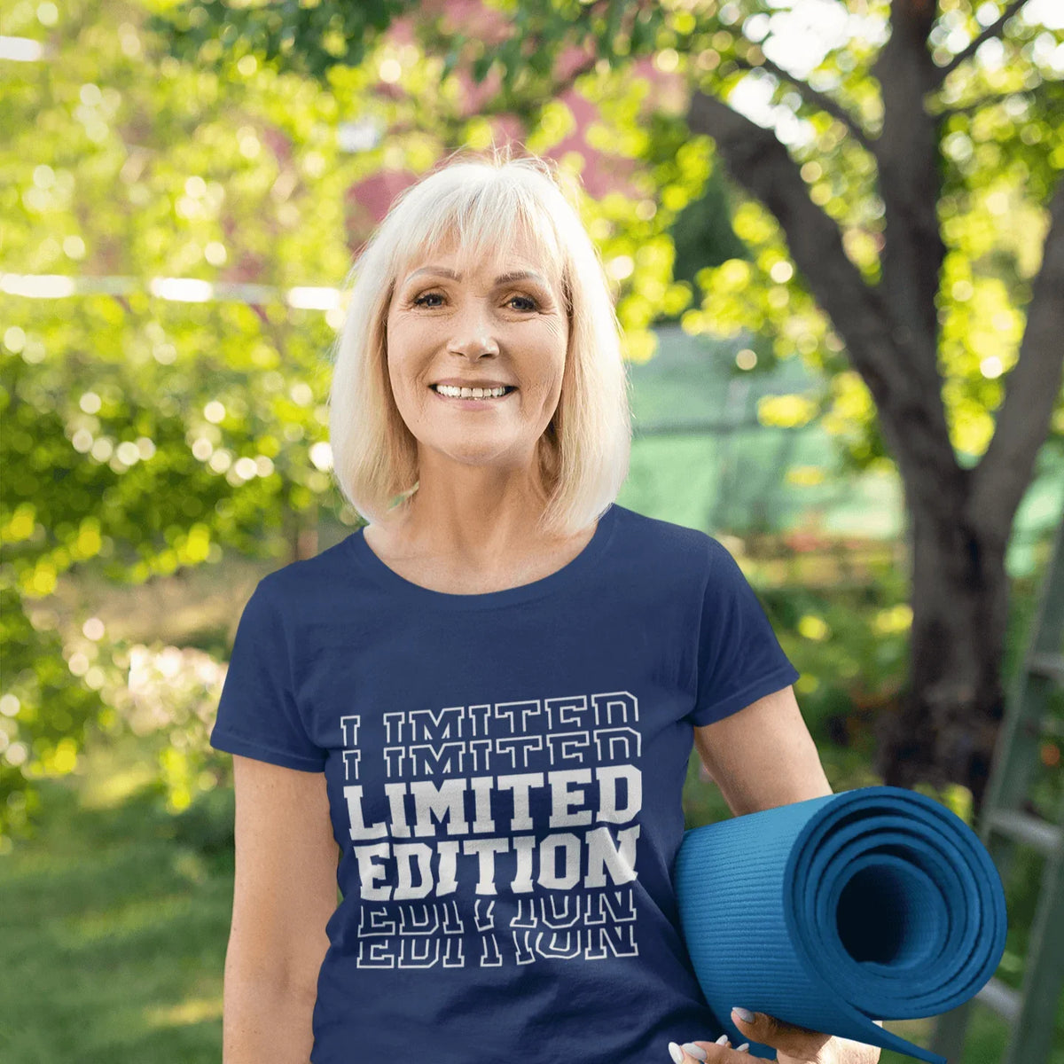 Woman in navy 'Limited Edition' tee holding yoga mat outdoors, soft graphic tee for birthdays & trips