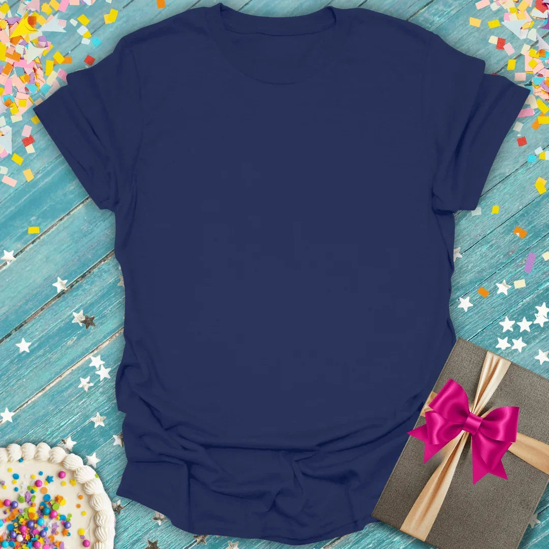 Navy blue tee with birthday cake, gift box, and confetti on teal wood — perfect for celebrations and gifts