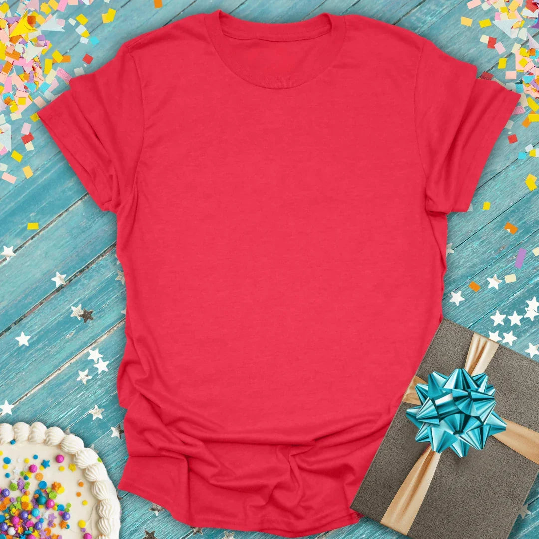 Red soft tee with birthday cake, gift box, and confetti on blue wood — perfect for celebrations and trips