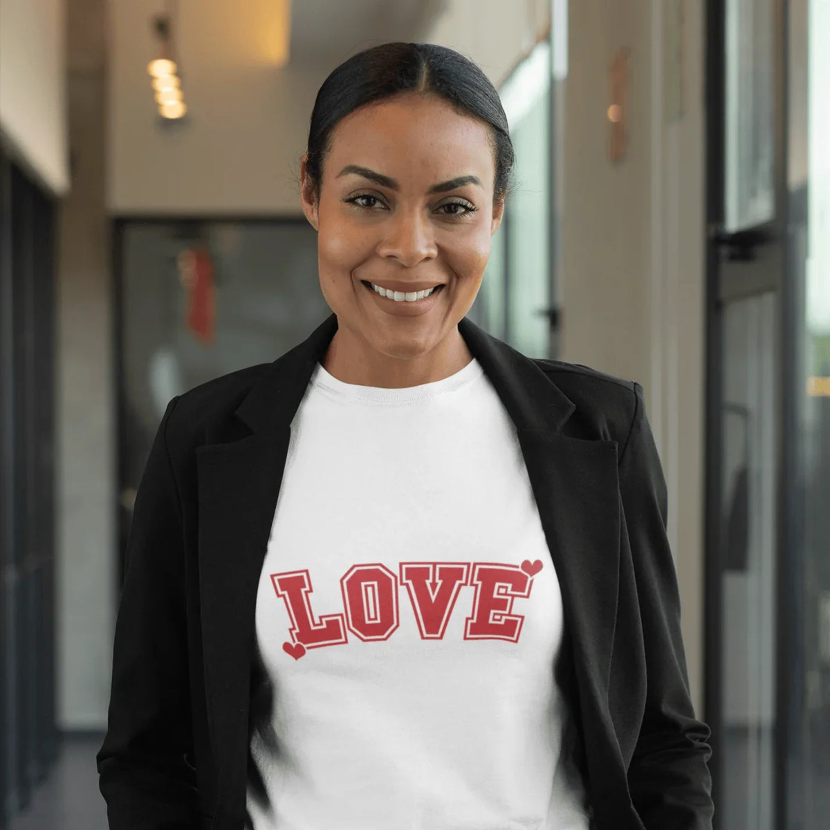 Woman smiling in white tee with red 'LOVE' graphic and hearts, styled with black blazer for casual or gift wear