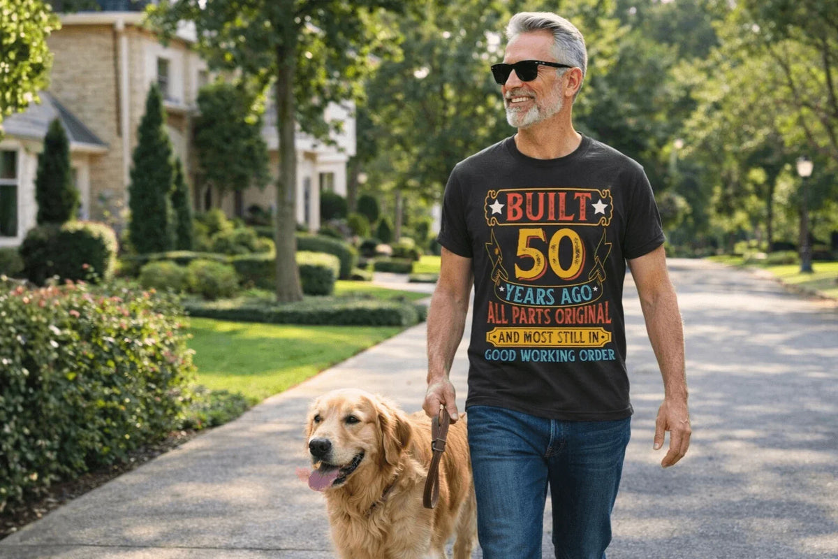 Man walking golden retriever wearing 50th birthday tee: 'Built 50 Years Ago, All Parts Original'