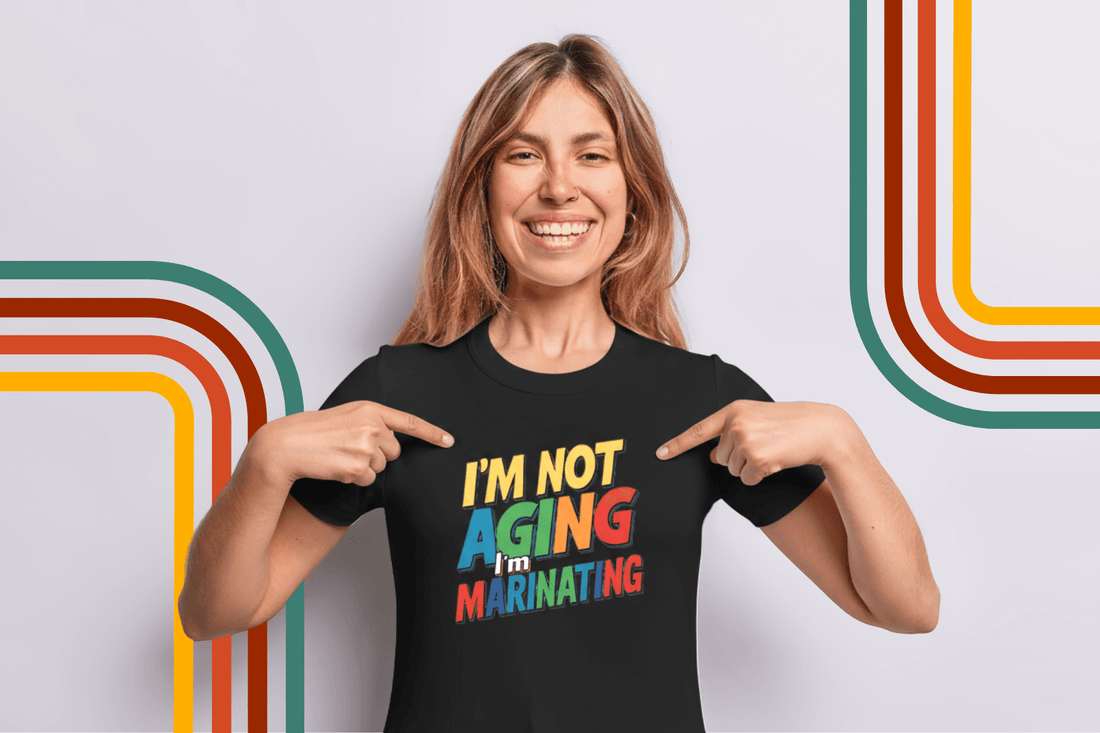 Woman smiling in black tee with colorful 'I'm not aging, I'm marinating' text, pointing at design