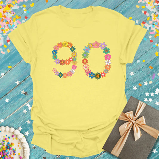 Yellow 90th birthday T-shirt with floral number design, confetti, cake, and gift box