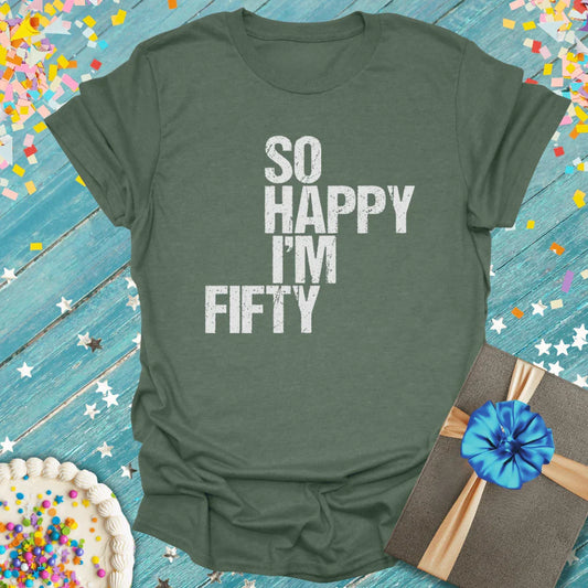 Green 'So Happy I'm Fifty' birthday T-shirt with cake, gift box, and confetti on blue wood