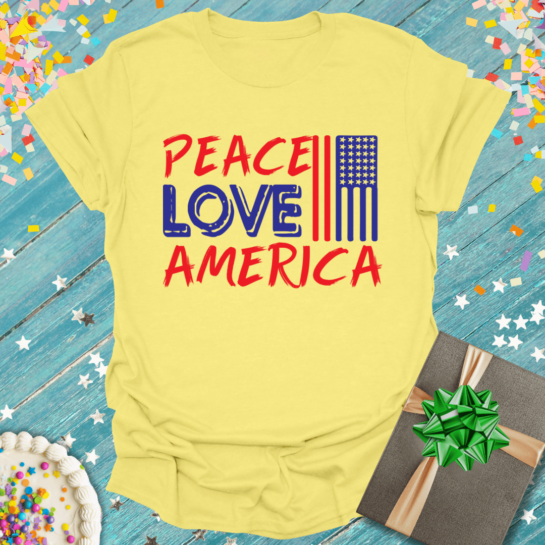 Yellow Peace Love America tee with flag design, gift box, and birthday cake on blue wood