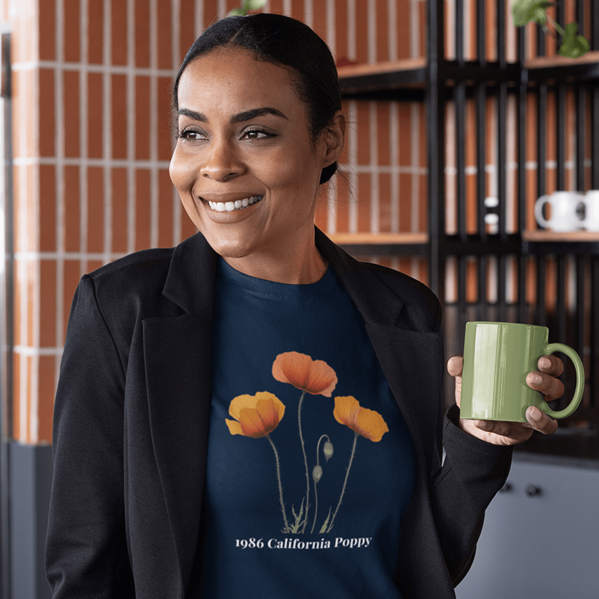 Woman smiling in navy tee with 1986 California Poppy floral design, holding green mug, perfect for birthdays or trips.