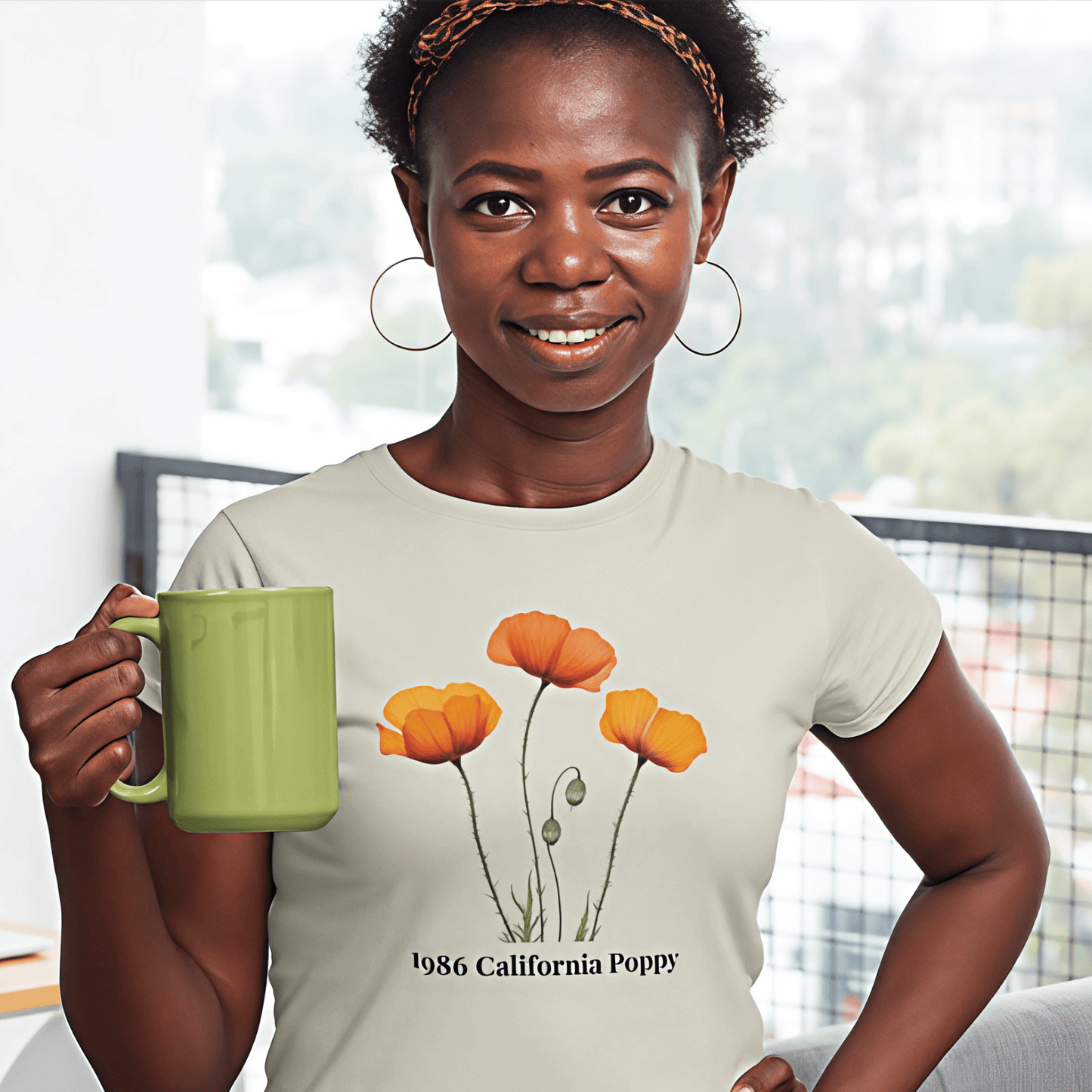 Woman wearing 1986 California Poppy tee, holding green mug, smiling indoors