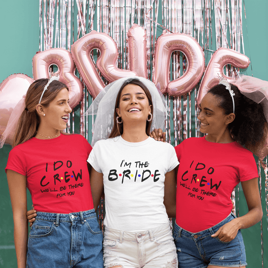 Bride and bridesmaids in fun wedding tees, 'I'm the Bride' and 'I Do Crew,' celebrating with pink balloons and veils.
