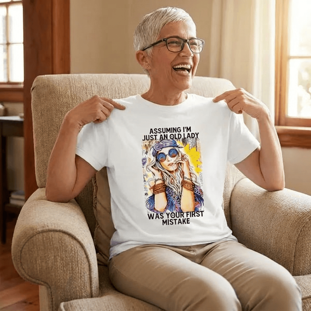 Woman wearing funny 'Assuming I'm just an old lady was your first mistake' graphic tee, laughing in armchair