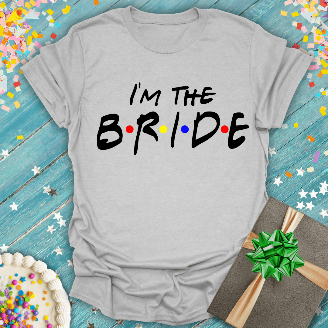 Gray 'I'm The Bride' tee with colorful dots, on blue wood with confetti, cake, and gift—perfect for bridal celebrations.