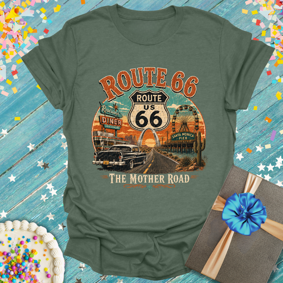 An military green graphic t-shirt featuring a vintage-style 'Route 66 The Mother Road' print, displayed on a rustic blue wooden background with confetti, a cake, and a gift box.