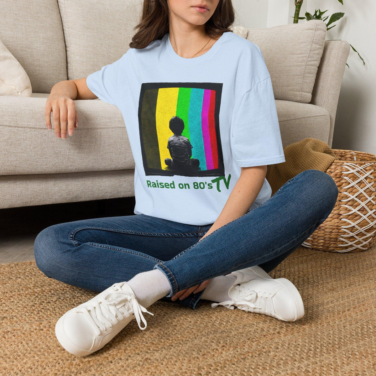 Light blue 'Raised on 80's TV' tee by Epic Era Tees featuring retro test pattern graphic with child silhouette and green text.