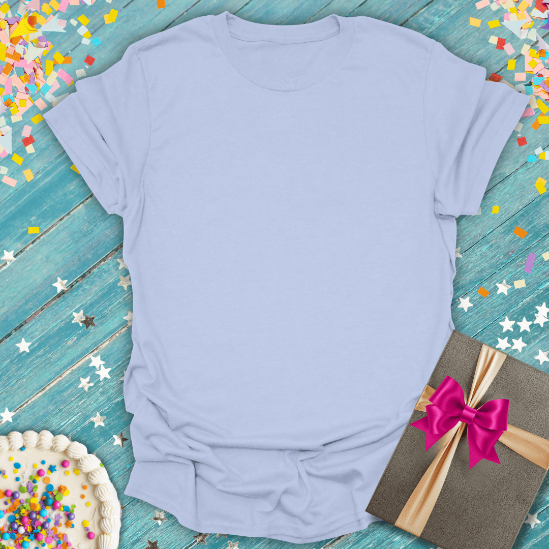 Soft lavender t-shirt with birthday cake, gift box, and confetti on teal wood — perfect for celebrations and trips