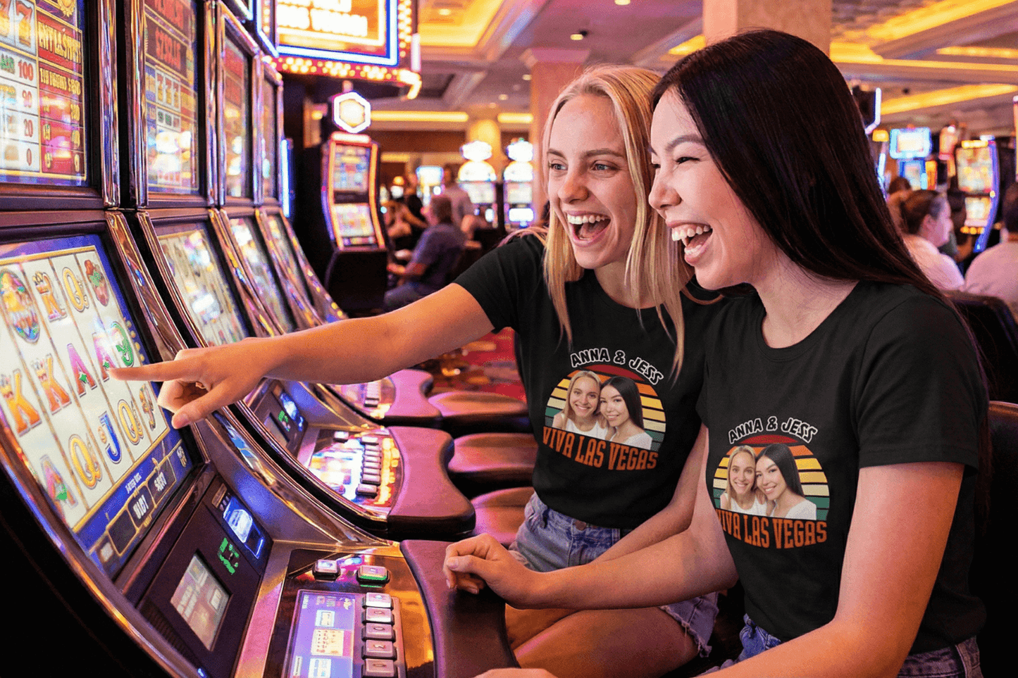 Two women laughing at slot machines in Vegas, wearing custom 'Viva Las Vegas' photo tees for trips and birthdays