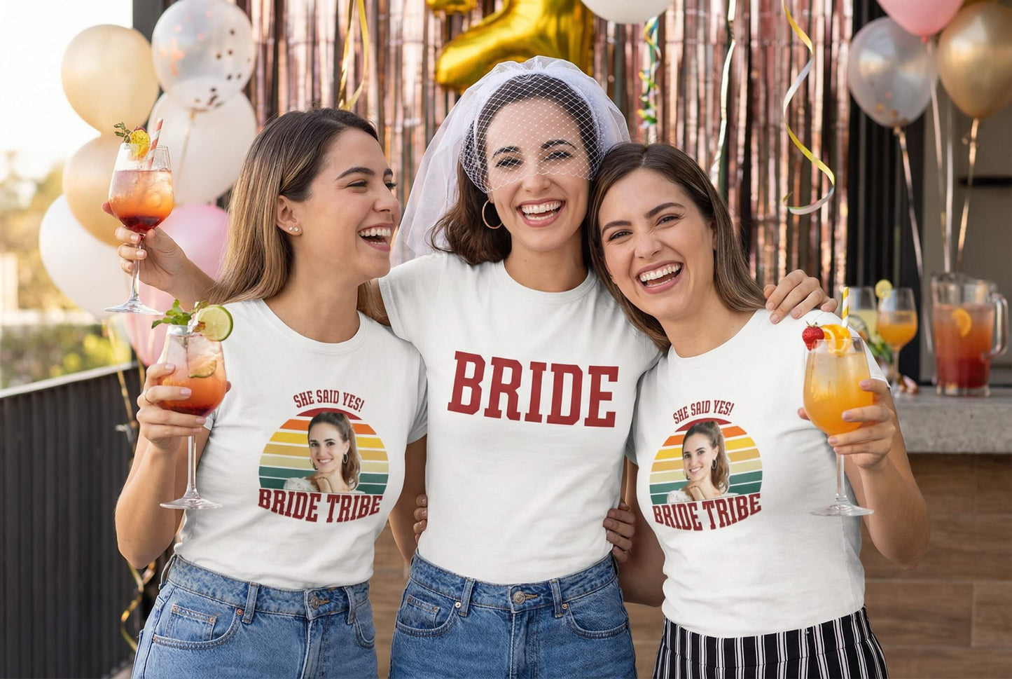 Bride and bridesmaids in matching 'Bride Tribe' tees celebrating with cocktails at a party
