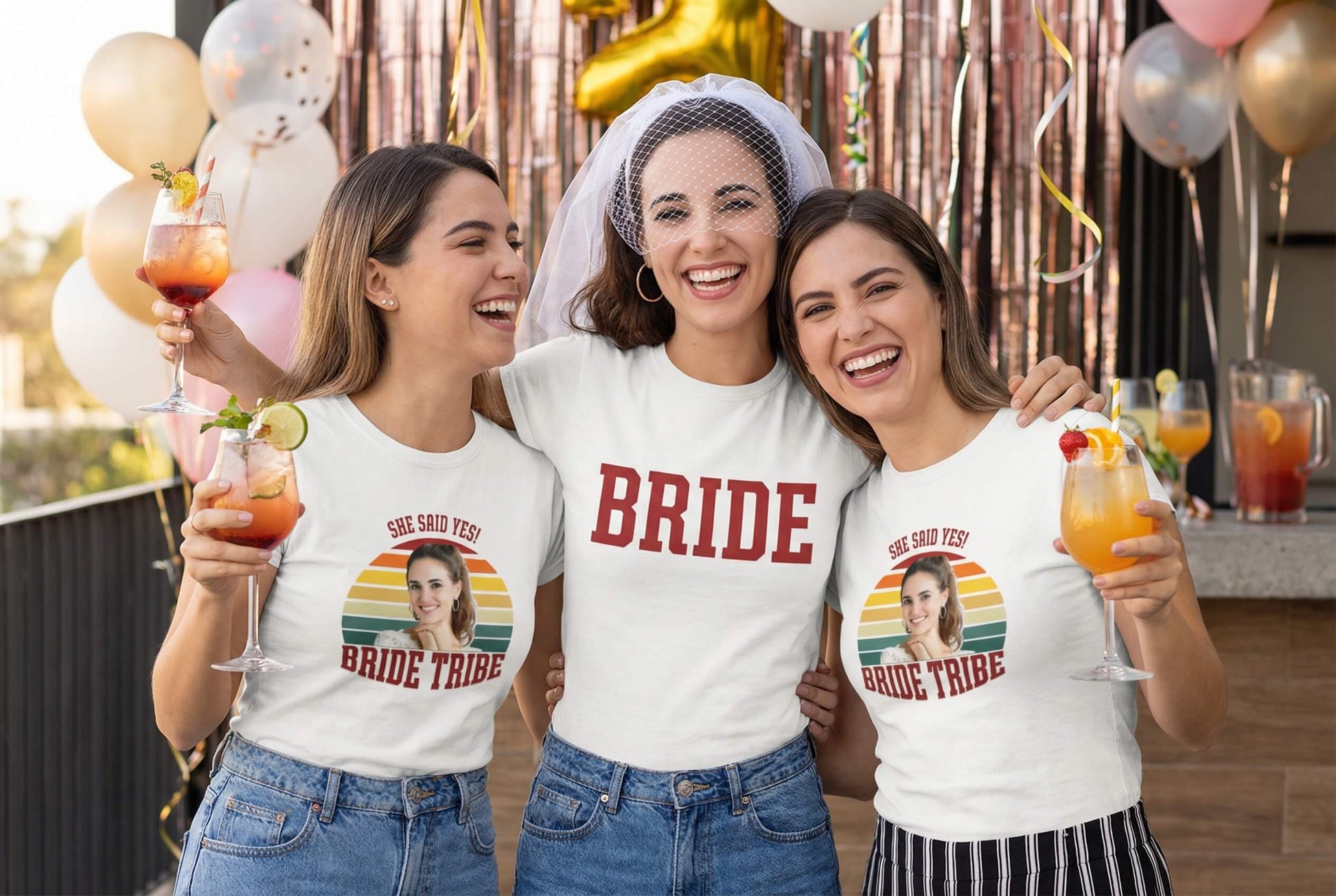 Bride and bridesmaids in matching 'Bride Tribe' tees celebrating with cocktails at a party