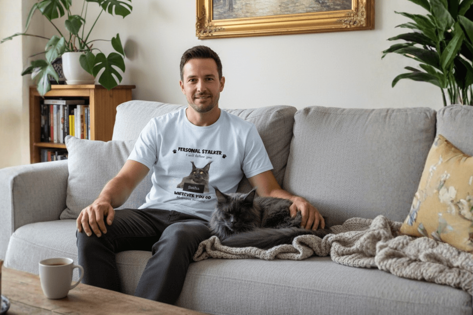 Man wearing funny cat lover tee with 'Personal Stalker' print, relaxing on couch with fluffy gray cat.