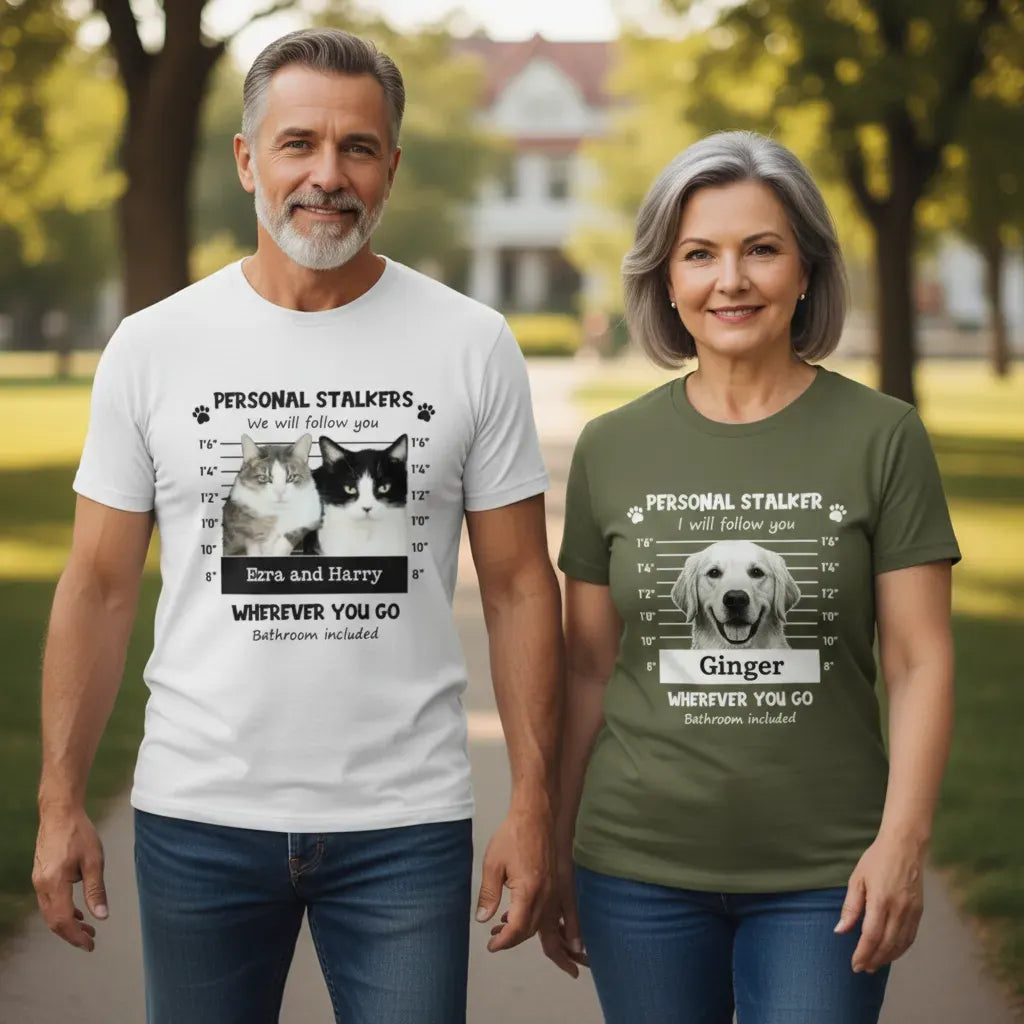 A couple walking together wearing custom 'Personal Stalker' and 'Mugshot' t-shirts featuring their cats, Ezra and Harry, after their viral bathroom stalking incident.